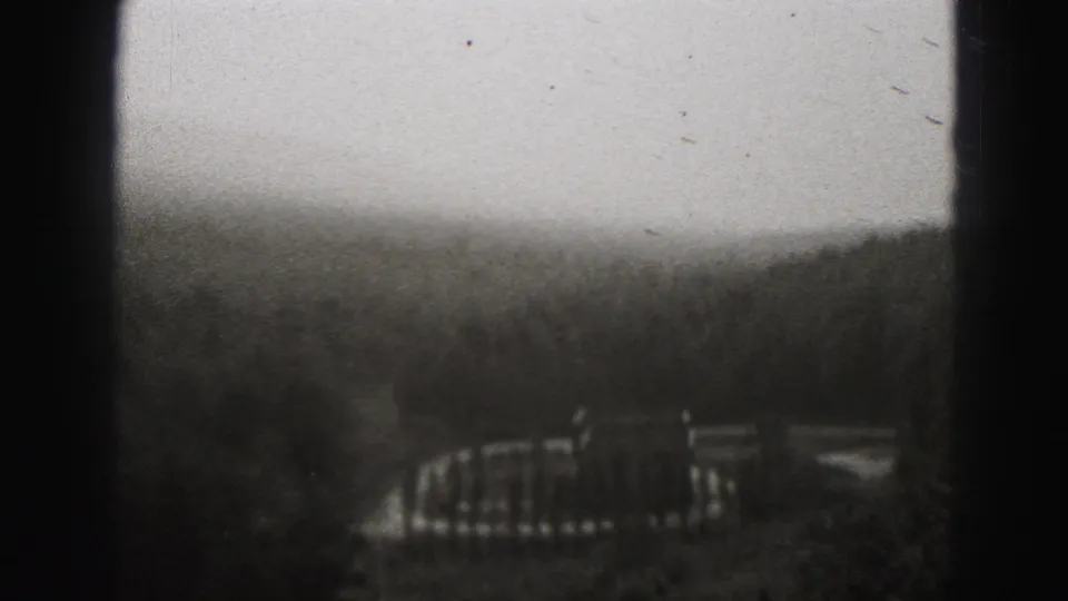 1975 Harrisburg-area 8mm frame showing a hazy wooded hillside and distant built feature under a pale sky.
