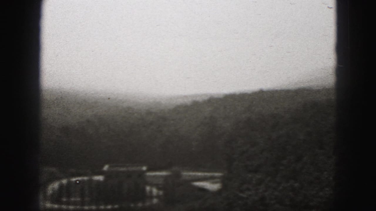 Distant structures among trees beneath a pale sky, partly obscured by frame borders.