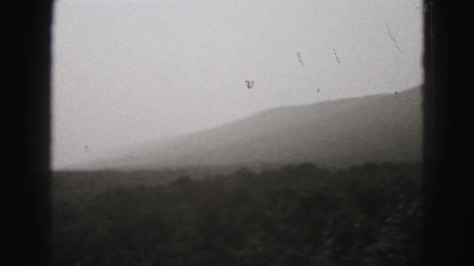1975 8mm landscape frame from the Harrisburg-area clip, with layered hills and dark foreground vegetation.