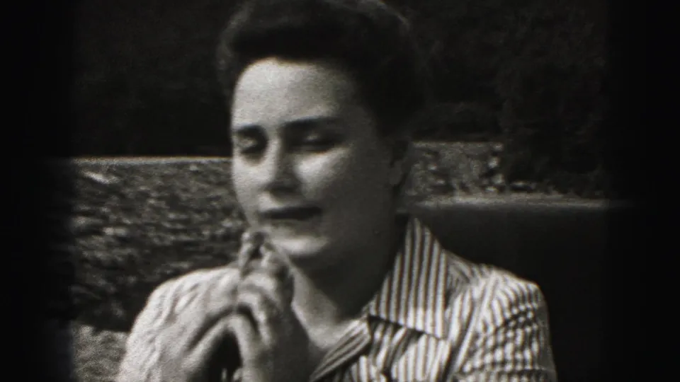 In metadata-supported 1975 Harrisburg home-movie footage, a woman in a striped shirt raises a handkerchief near her face outdoors.