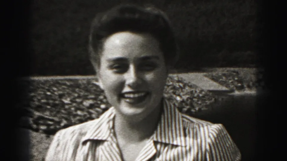 A woman in a striped collared shirt smiles toward the camera in the 1975 Harrisburg home-movie setting.
