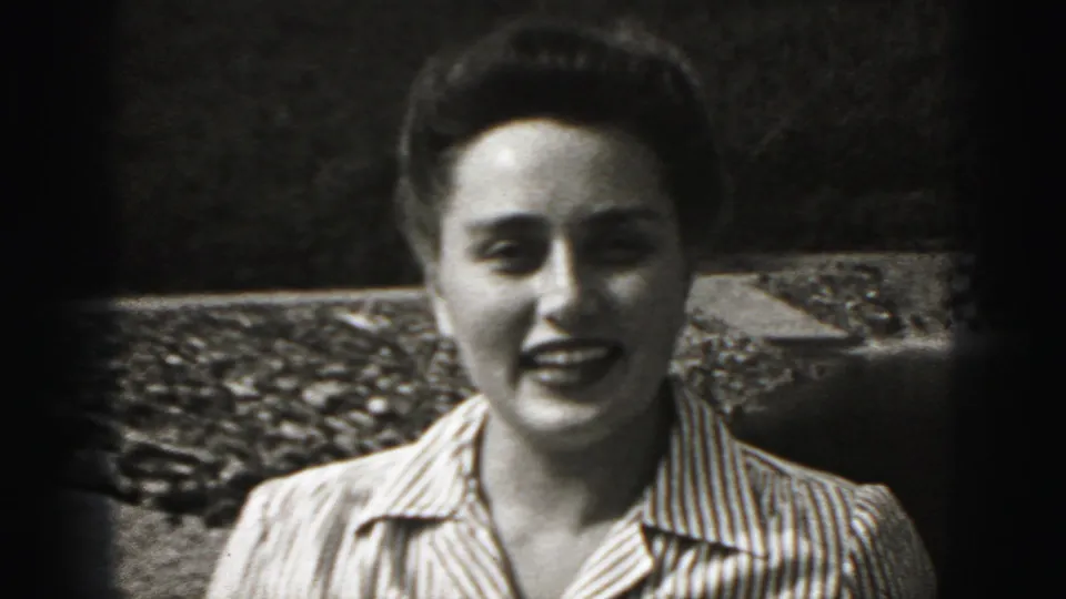 The woman remains centered and smiling in a grainy 8mm close-up, with outdoor stonework behind her.
