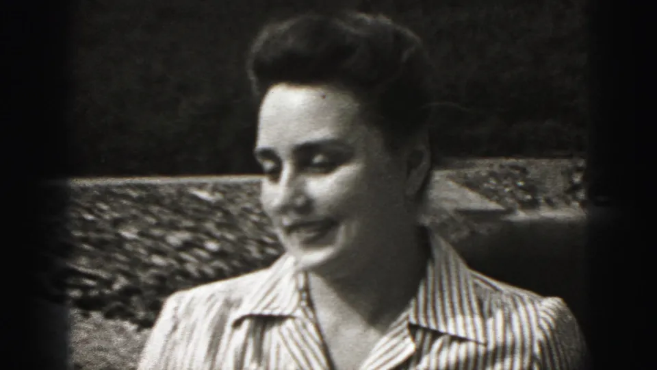 The woman turns in profile beside the low stone wall, still framed as an informal outdoor home-movie portrait.
