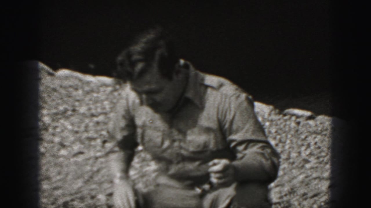 The man crouches outdoors on gravel in the Harrisburg 1975 home-movie clip, looking down as the puppy moves out of clear view.