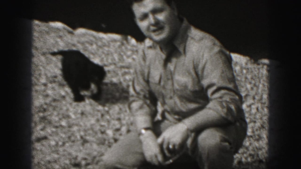 Adult man crouching on gravel beside a small dark dog.