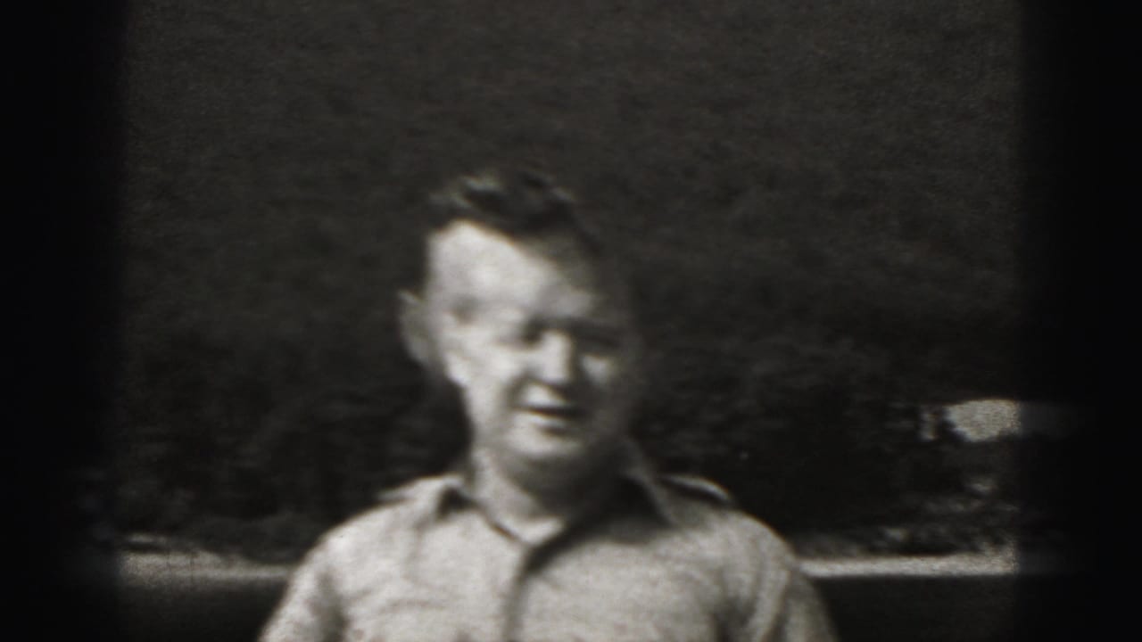 Man in a military-style shirt smiling outdoors in grainy black-and-white footage.