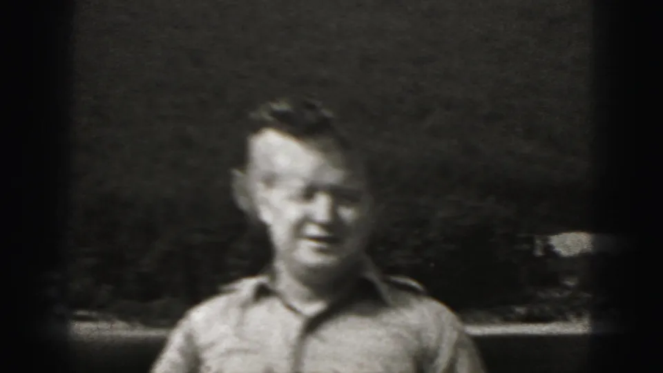 A man in a collared military-style shirt faces the camera outdoors in 1975 Harrisburg home-movie footage.