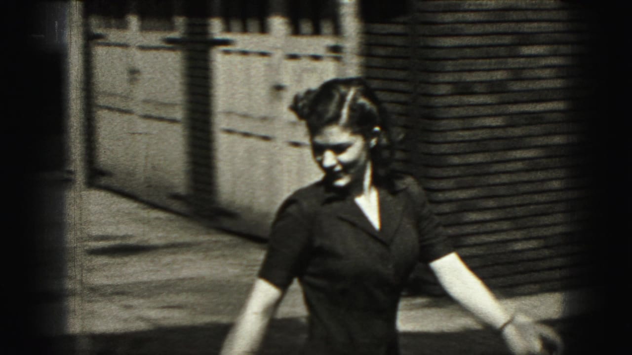 Woman in a dark dress walking near a brick exterior and fence.
