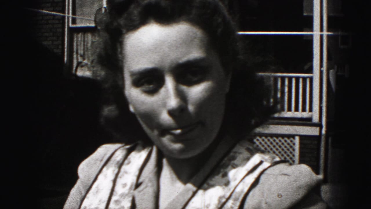 Young woman in sunlight looks toward the camera beside a porch railing and brick wall.