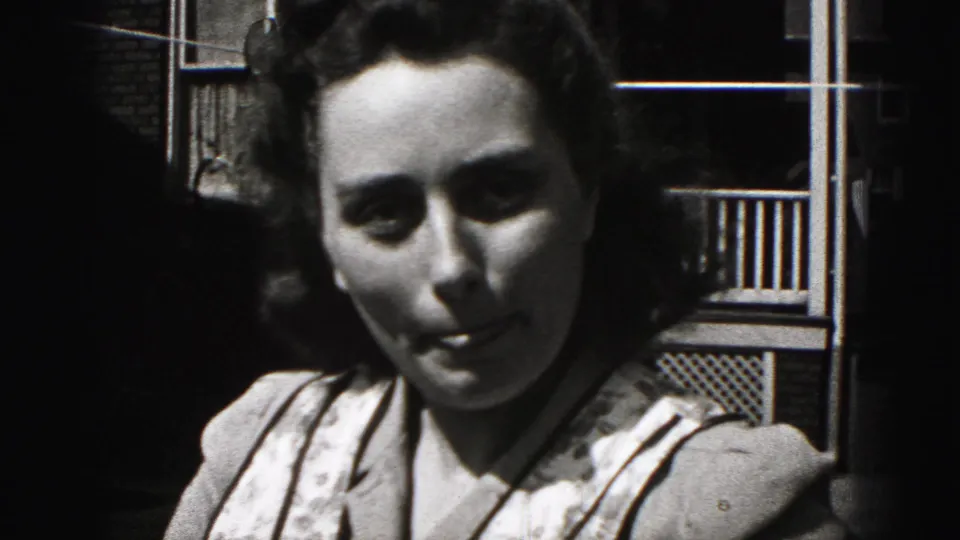 Close 1975 Harrisburg home-movie frame of a young woman with dark curled hair facing the camera on a shaded porch.