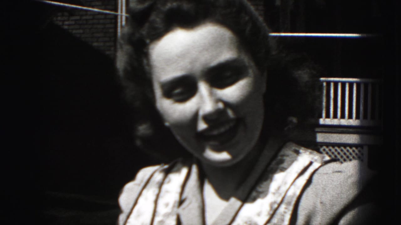 Close 1975 Harrisburg 8mm frame of the woman turning toward the camera with a slight smile near a porch railing.