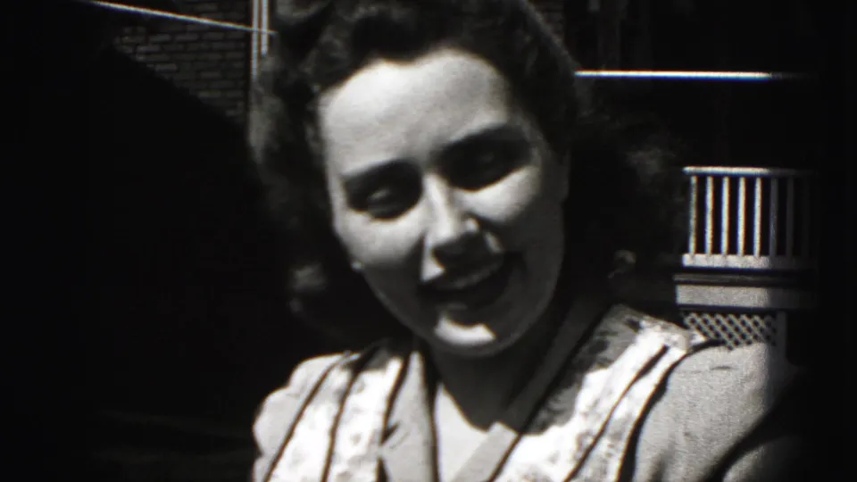 Close 1975 Harrisburg 8mm frame of the woman turning toward the camera with a slight smile near a porch railing.