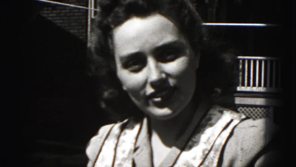 1975 Harrisburg home-movie frame showing the young woman smiling with parted lips in a close outdoor porch portrait.