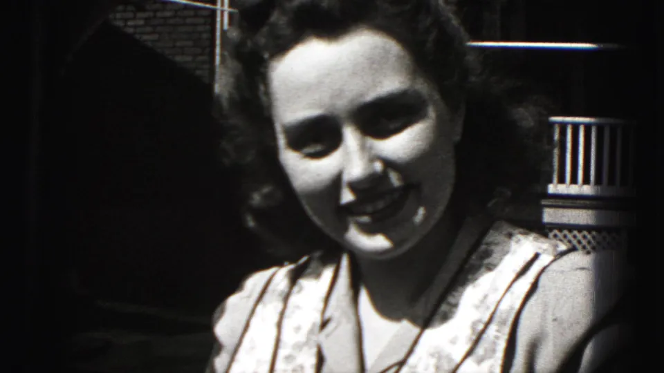 Close 1975 Harrisburg 8mm frame of the woman smiling warmly at the camera against porch railing and brickwork.