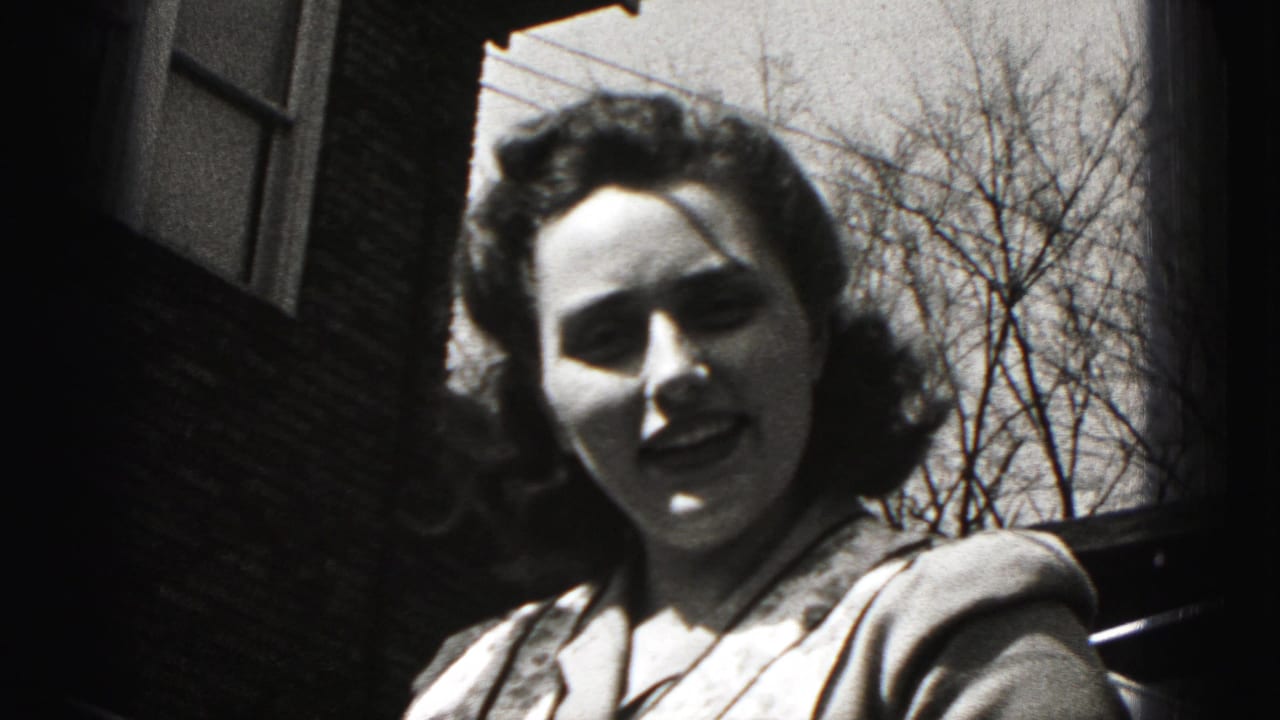 Woman faces the camera outdoors with bare trees and a brick building behind her.