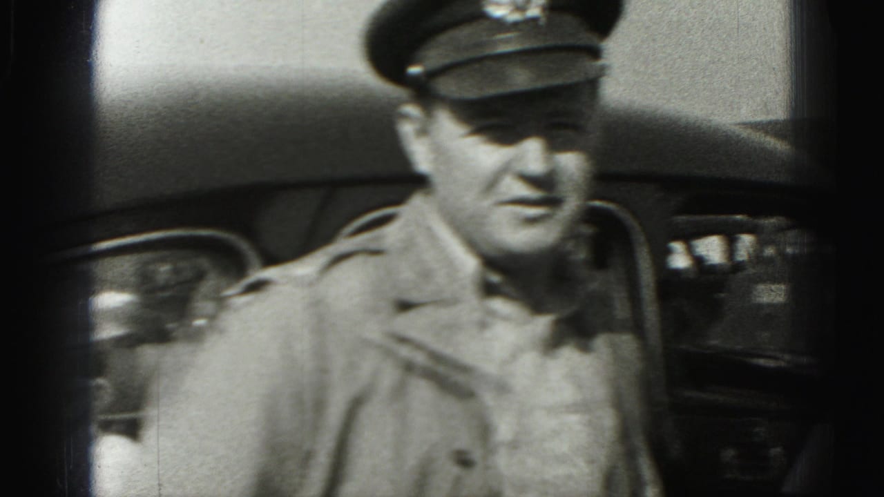 In 1975 Harrisburg home-movie footage, a uniformed man in a peaked cap stands near a vintage car and looks toward the camera.