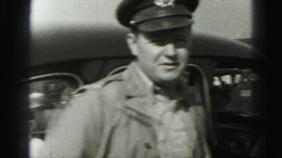 In 1975 Harrisburg home-movie footage, a uniformed man in a peaked cap stands near a vintage car and looks toward the camera.