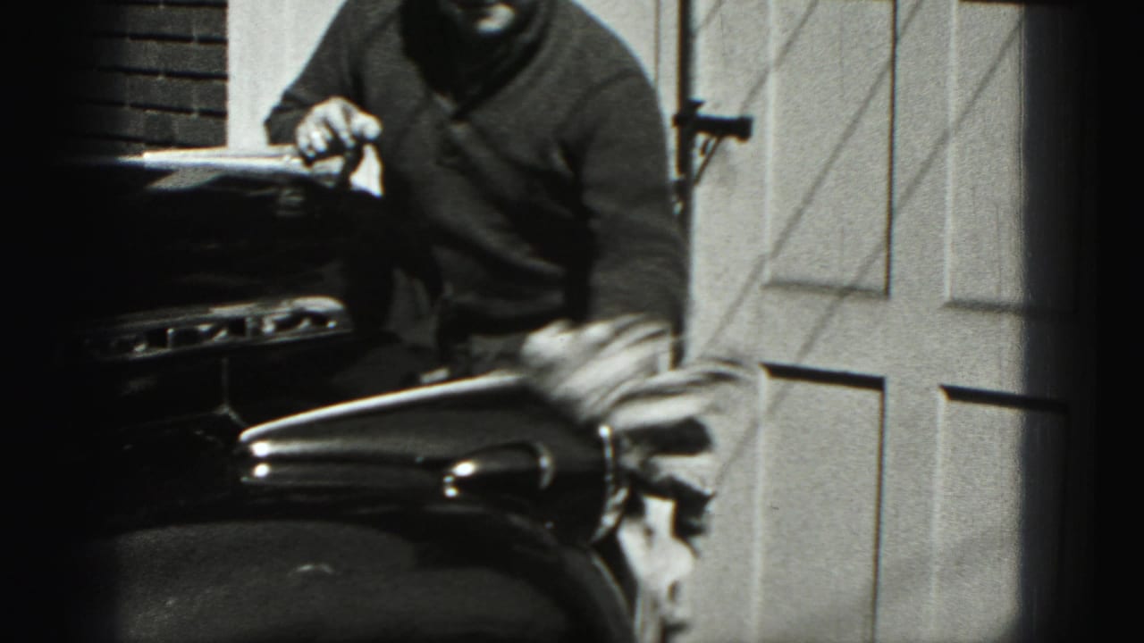 A man in a dark sweater stands beside a classic car during a 1975 Harrisburg driveway car-cleaning moment.