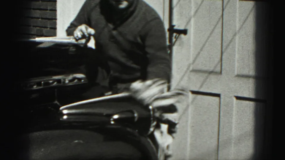 A man in a dark sweater stands beside a classic car during a 1975 Harrisburg driveway car-cleaning moment.