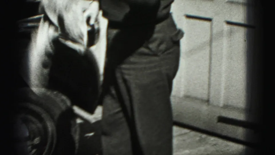 The man stands beside the car near the paneled garage door, with a cloth visible as he finishes or pauses during the wash.