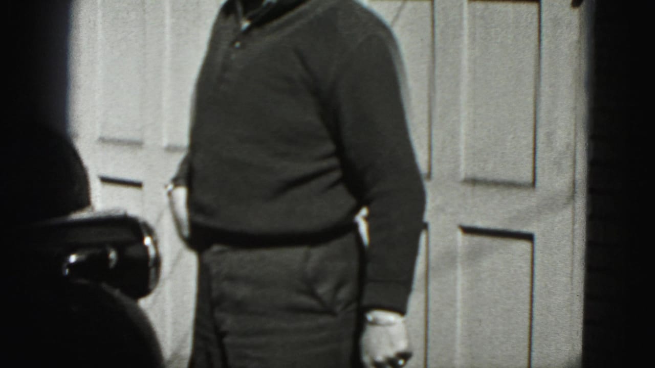 Man beside a classic car in front of a paneled garage door.