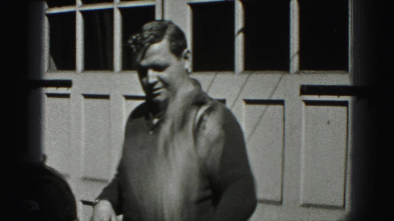 Adult man faces the camera near a paneled garage door during 1975 Harrisburg home-movie footage of car waxing.