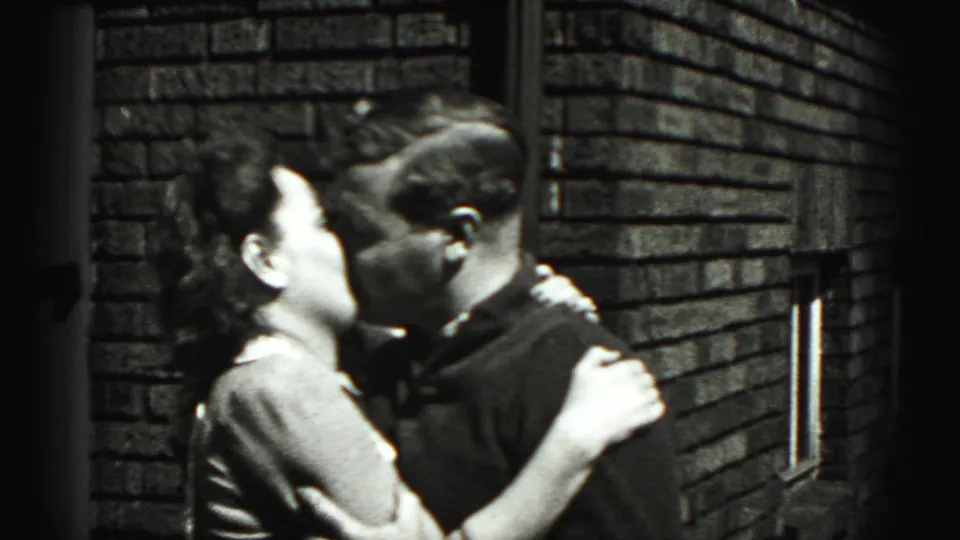 The couple remain close together by the brick building, with the woman turned toward the man in the supplied 1975 Harrisburg footage.