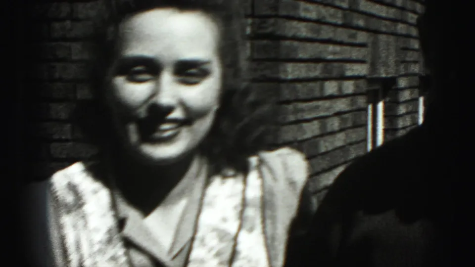 A closer home-movie frame shows the young woman smiling near the brick building, with the man partly cropped at the edge.