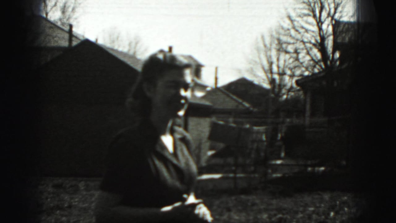 A woman stands in a grassy Harrisburg backyard in 1975 home-movie footage, with houses and bare trees in the background.