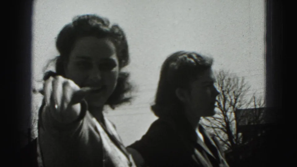 A woman gestures or waves toward the camera in a 1975 Harrisburg outdoor home-movie frame while another person stands beside her.