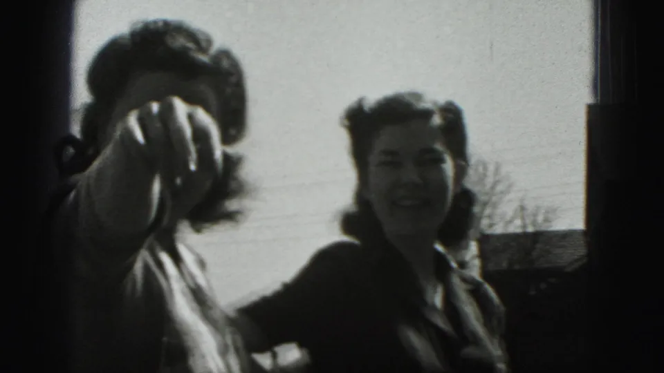 In 1975 Harrisburg home-movie footage, two adult women stand outside as one gestures near the lens and the other smiles.