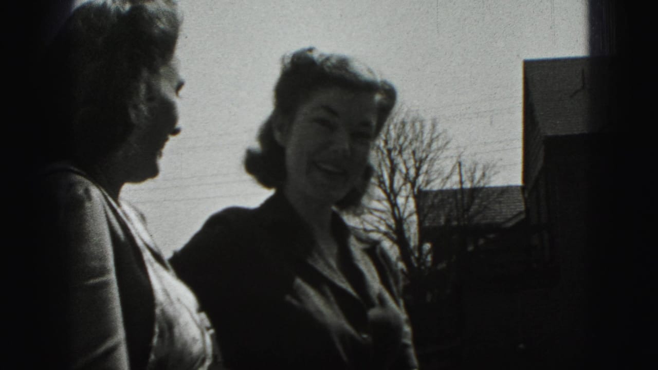 Two adult women in 1975 Harrisburg stand outside laughing, with bare trees and house roofs behind them.