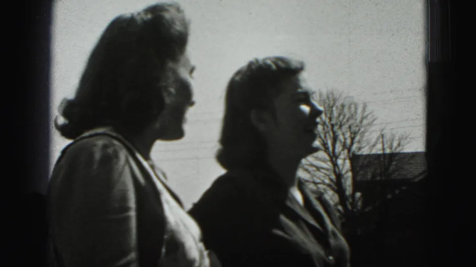 The two women continue their outdoor conversation in Harrisburg, with soft 8mm focus and a residential background.