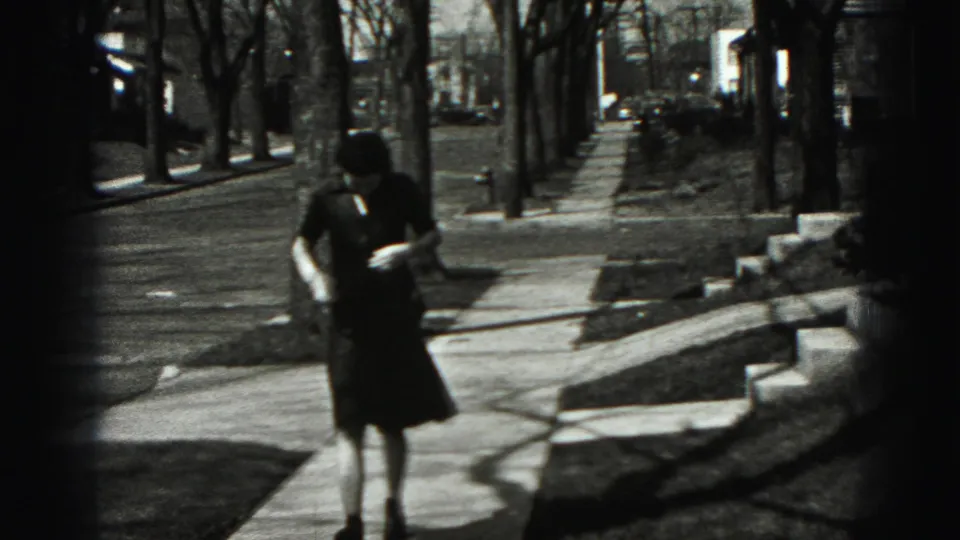 Adult woman in a dark dress appears to adjust her jacket while walking on a Harrisburg residential sidewalk.