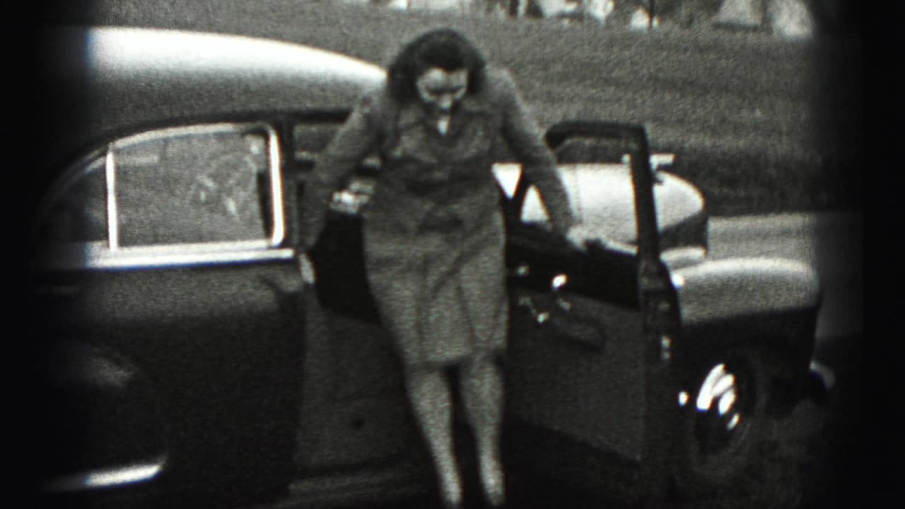 Woman stepping from an open car door beside a parked sedan in a grassy outdoor setting.
