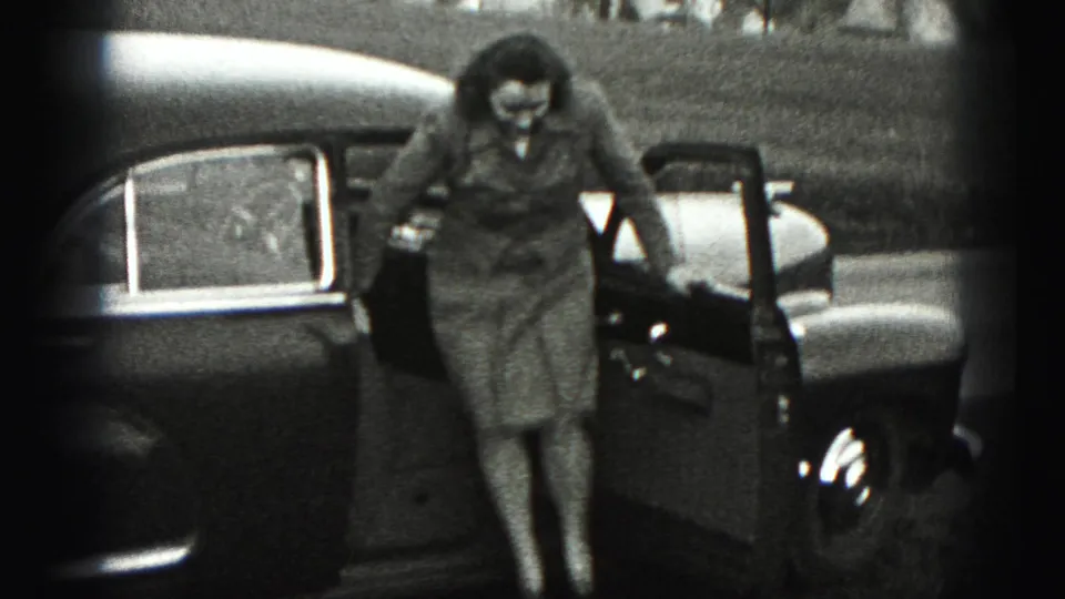 In 1975 Harrisburg home-movie footage, a woman steps out of an open sedan door beside a grassy field.