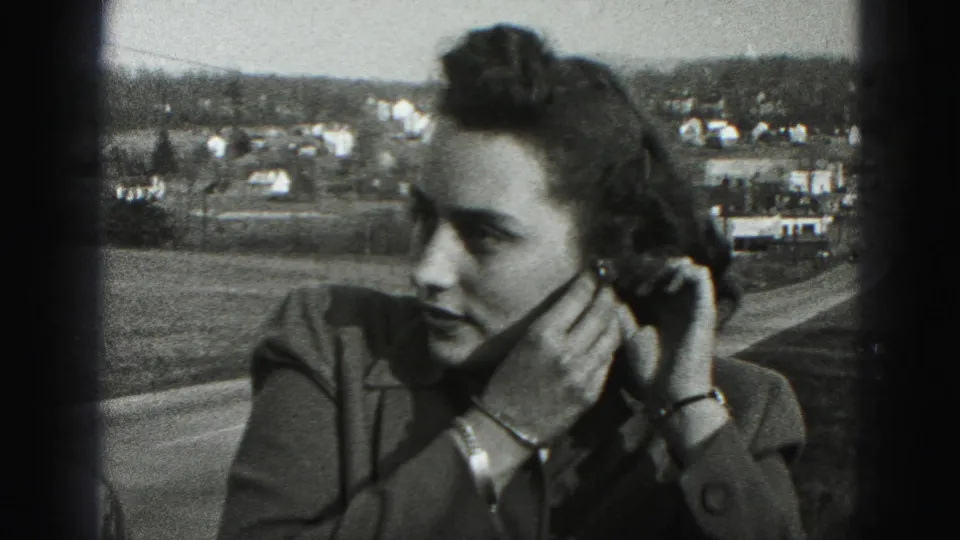 The woman turns in profile while holding her earring, with a Harrisburg-area road and distant homes visible behind her.