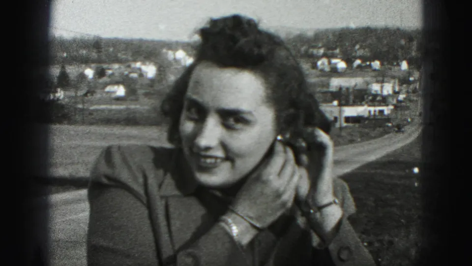 The woman smiles broadly with both hands near her earring, framed by 8mm film edges and a Harrisburg-area roadside view.