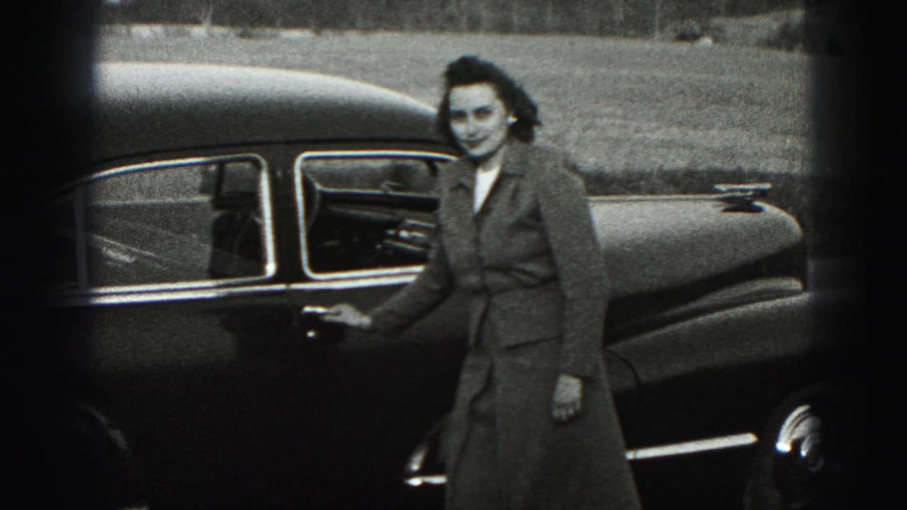In Harrisburg, Pennsylvania, a woman in a mid-1970s coat stands by a dark sedan in grainy black-and-white 8mm footage.
