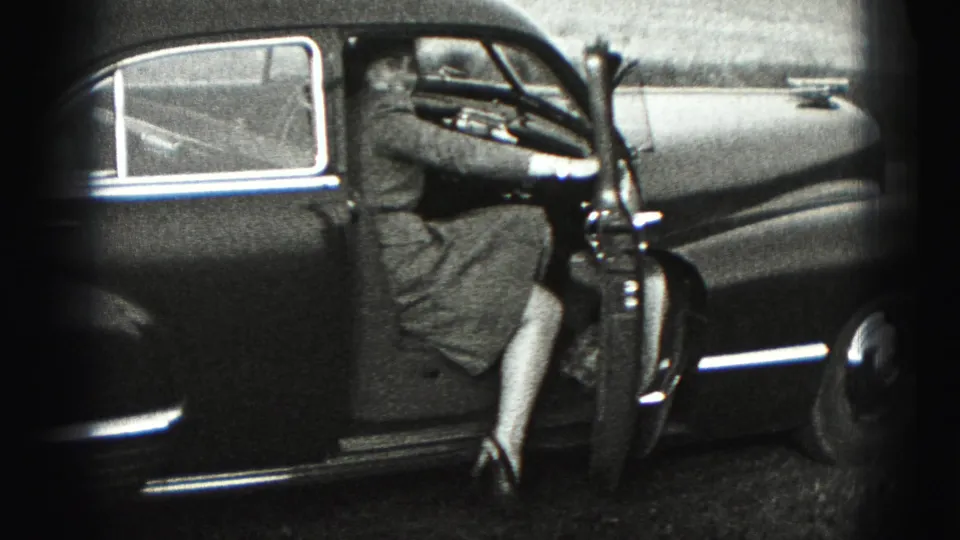 The woman steps into the older sedan in the 1975 Harrisburg home-movie scene, partially turned away from the camera.