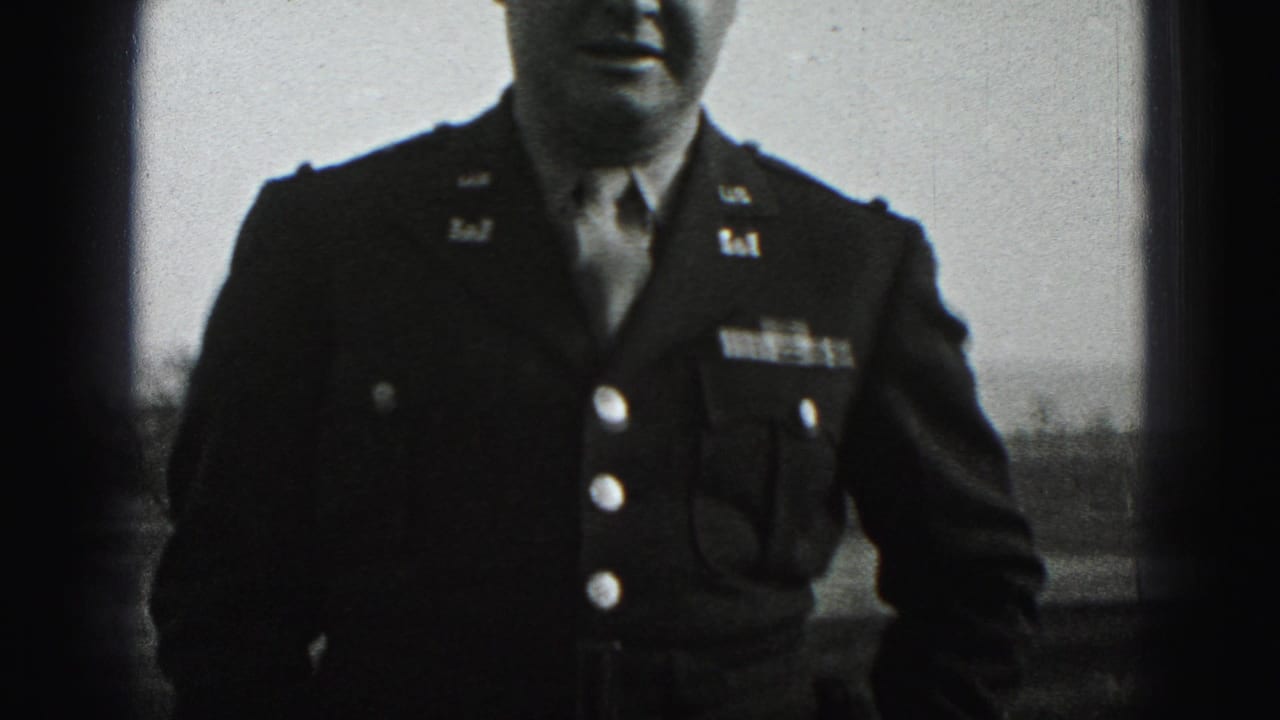 In Harrisburg, Pennsylvania home-movie footage from 1975, a man in a dark military-style jacket stands outdoors with insignia and buttons visible.