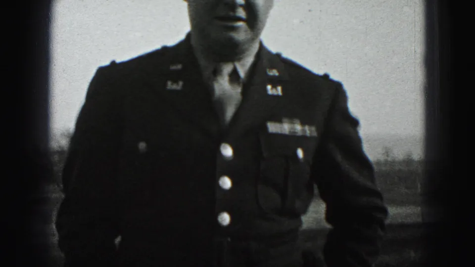 In Harrisburg, Pennsylvania home-movie footage from 1975, a man in a dark military-style jacket stands outdoors with insignia and buttons visible.