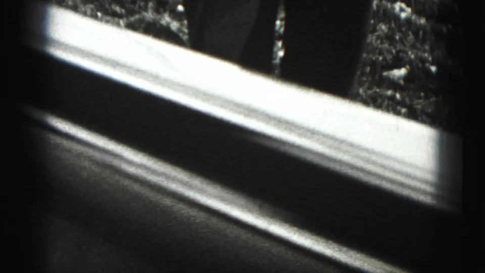 Close view of a reflective surface in 1975 Harrisburg home-movie footage, with blurred ground and partial legs visible.