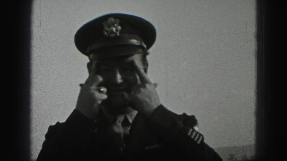 A uniformed adult man adjusts his peaked cap with both hands in the final 1975 Harrisburg home-movie frame.
