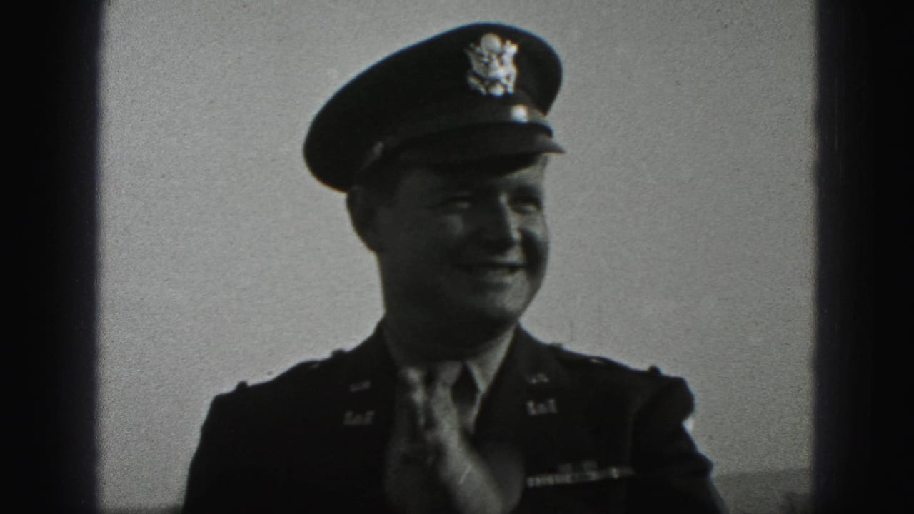 In 1975 Harrisburg home-movie footage, a uniformed soldier in a peaked cap smiles toward the camera while adjusting his tie.