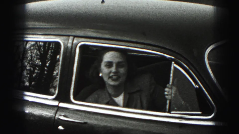 In Harrisburg metadata context, a woman in a collared jacket sits in a vintage car and faces the camera through the open window.