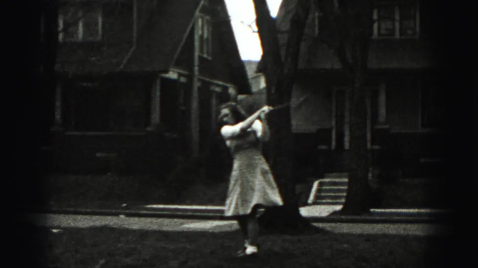 In a Harrisburg suburban yard, the woman stands with a golf club raised or angled near trees and large houses.