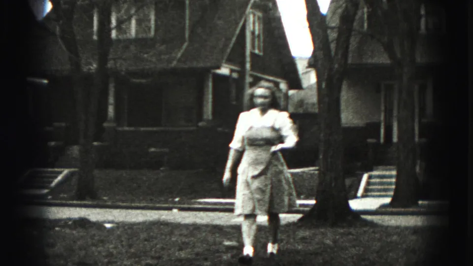 In Harrisburg, Pennsylvania home-movie footage, a woman walks across a yard with a golf club as houses and bare trees stand behind her.