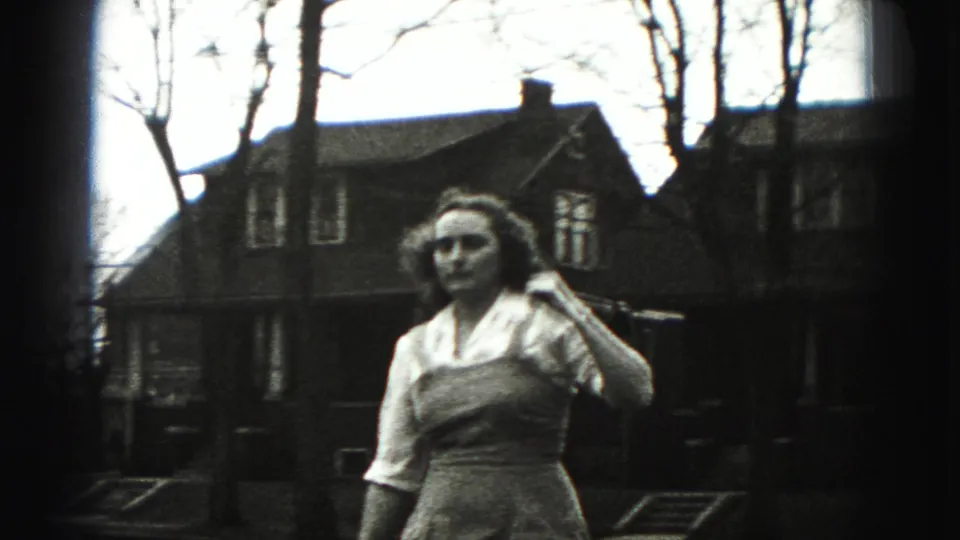 A closer Harrisburg home-movie frame shows the woman holding the golf club near her shoulder, with residential houses and leafless trees behind her.