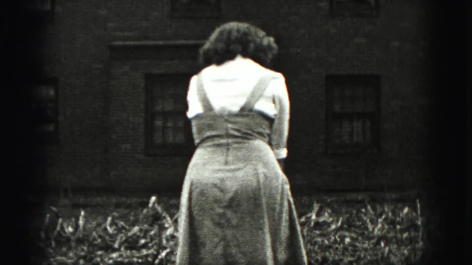 The woman faces away in a Harrisburg backyard, with a brick wall, windows, and low garden growth behind her.